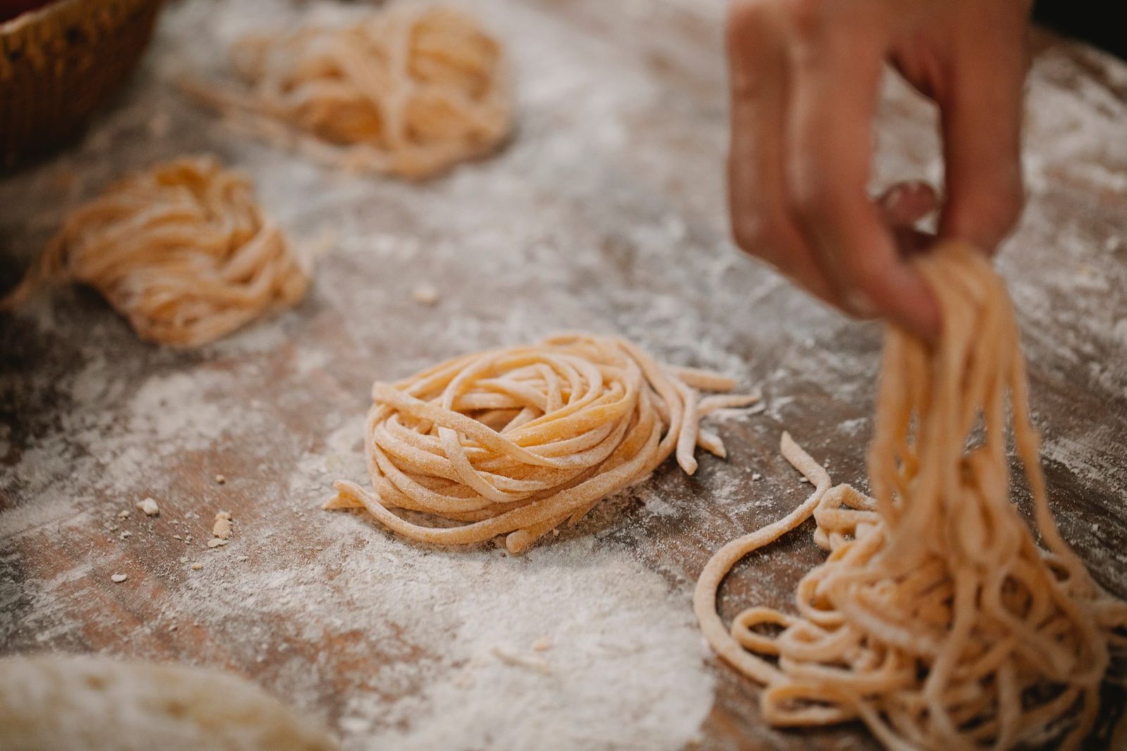 Mani che formano nidi di tagliatelle fresche su un tavolo cosparso di farina