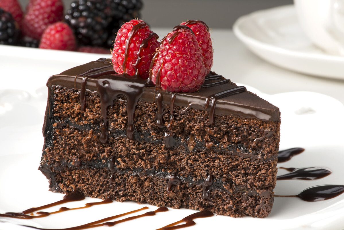 Fetta di torta al cioccolato con lamponi freschi e colata di cioccolato fondente