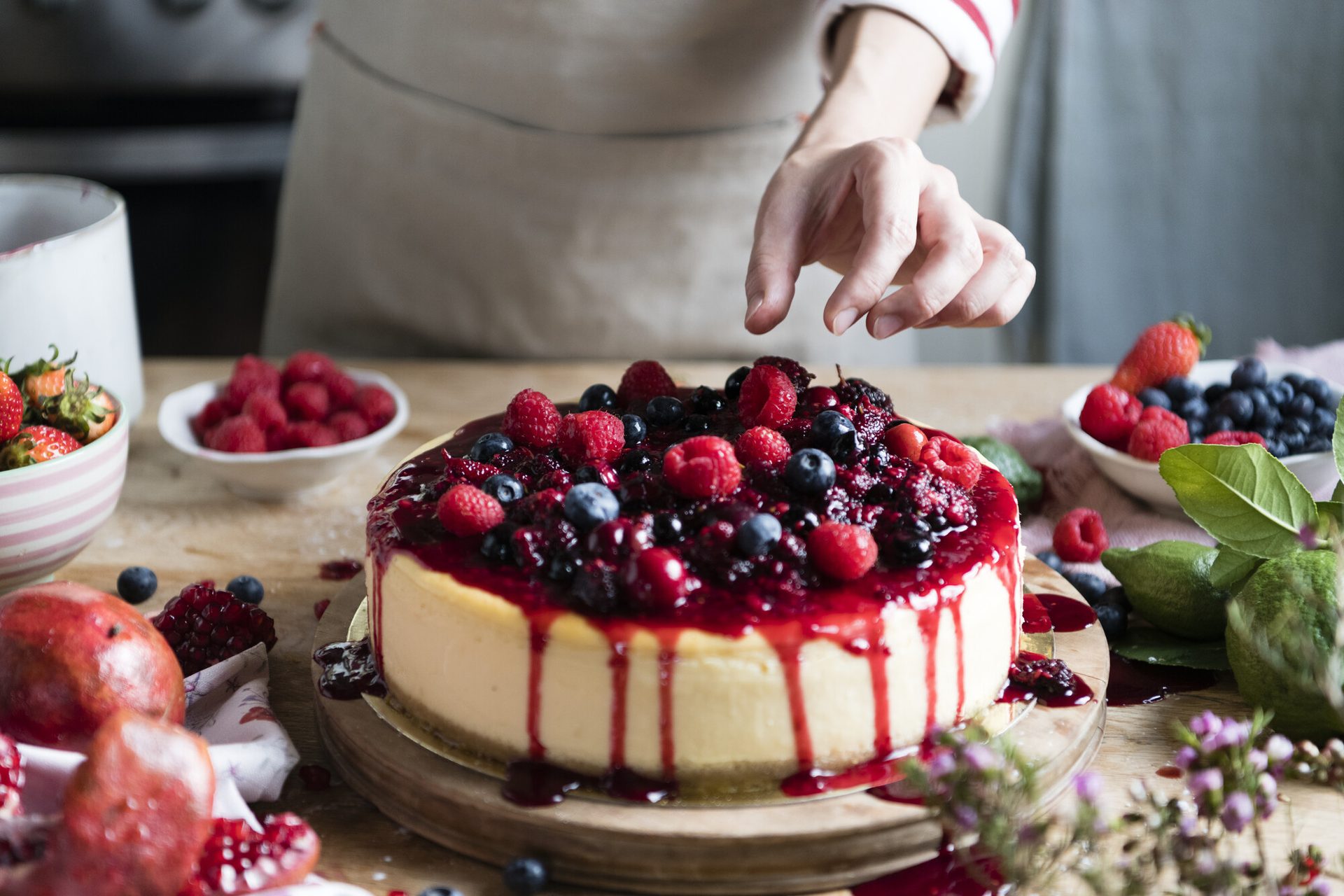 Mani che rifiniscono a mano una torta ai frutti di bosco sul banco del laboratorio